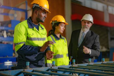 Kıdemli müdür kadrolu mühendis kadın ve Afrikalı adamla birlikte denetleme yapıyor. Fabrika binasının inşaat yapısını kontrol ediyorlar. Çelik çatı yapısı ve makine kurulumu olan depo.