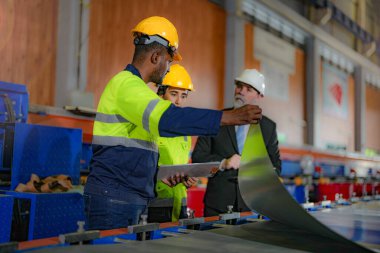 Kıdemli müdür kadrolu mühendis kadın ve Afrikalı adamla birlikte denetleme yapıyor. Fabrika binasının inşaat yapısını kontrol ediyorlar. Çelik çatı yapısı ve makine kurulumu olan depo.