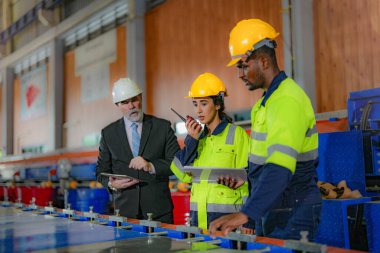 Kıdemli müdür kadrolu mühendis kadın ve Afrikalı adamla birlikte denetleme yapıyor. Fabrika binasının inşaat yapısını kontrol ediyorlar. Çelik çatı yapısı ve makine kurulumu olan depo.