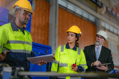 Kıdemli müdür kadrolu mühendis kadın ve Afrikalı adamla birlikte denetleme yapıyor. Fabrika binasının inşaat yapısını kontrol ediyorlar. Çelik çatı yapısı ve makine kurulumu olan depo.