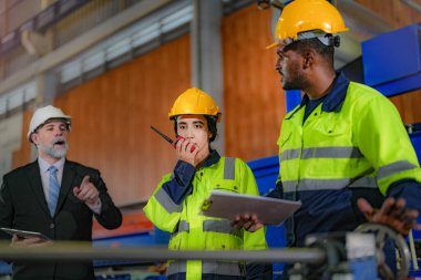 Kıdemli müdür kadrolu mühendis kadın ve Afrikalı adamla birlikte denetleme yapıyor. Fabrika binasının inşaat yapısını kontrol ediyorlar. Çelik çatı yapısı ve makine kurulumu olan depo.