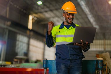 Fabrika mühendisi Afrikalı adam dizüstü bilgisayarla kendine güveniyor. İşçi, sanayi fabrikasındaki ağır makinede çalışıyor. Makine teçhizatı ile bitki teknolojisi.