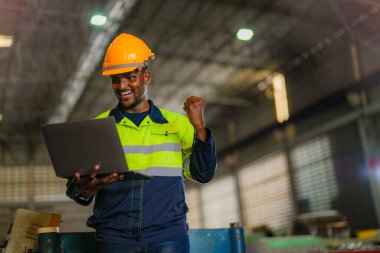 Fabrika mühendisi Afrikalı adam dizüstü bilgisayarla kendine güveniyor. İşçi, sanayi fabrikasındaki ağır makinede çalışıyor. Makine teçhizatı ile bitki teknolojisi.