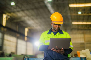 Fabrika mühendisi Afrikalı adam dizüstü bilgisayarla kendine güveniyor. İşçi, sanayi fabrikasındaki ağır makinede çalışıyor. Makine teçhizatı ile bitki teknolojisi.