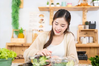 Gülümseyen kadın taze sağlıklı salata sebzeleri yiyor. Güzel bir iç mutfakta kilerde oturan bir kadın. Yerel ürünlerden ve malzemelerden alınan temiz diyet gıdaları taze pazardır..