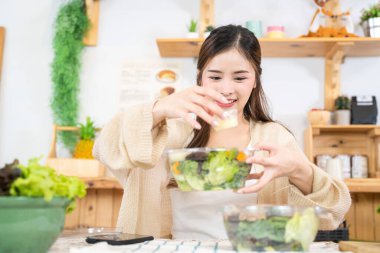 Gülümseyen kadın taze sağlıklı salata sebzeleri yiyor. Güzel bir iç mutfakta kilerde oturan bir kadın. Yerel ürünlerden ve malzemelerden alınan temiz diyet gıdaları taze pazardır..