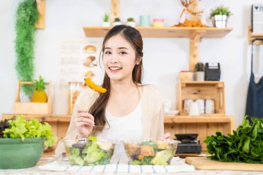 Gülümseyen kadın taze sağlıklı salata sebzeleri yiyor. Güzel bir iç mutfakta kilerde oturan bir kadın. Yerel ürünlerden ve malzemelerden alınan temiz diyet gıdaları taze pazardır..