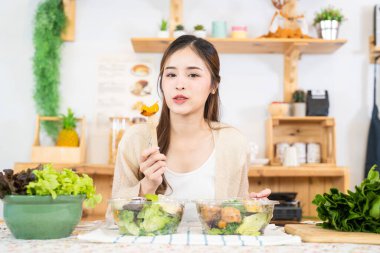 Gülümseyen kadın taze sağlıklı salata sebzeleri yiyor. Güzel bir iç mutfakta kilerde oturan bir kadın. Yerel ürünlerden ve malzemelerden alınan temiz diyet gıdaları taze pazardır..