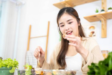 Gülümseyen kadın taze sağlıklı salata sebzeleri yiyor. Güzel bir iç mutfakta kilerde oturan bir kadın. Yerel ürünlerden ve malzemelerden alınan temiz diyet gıdaları taze pazardır..