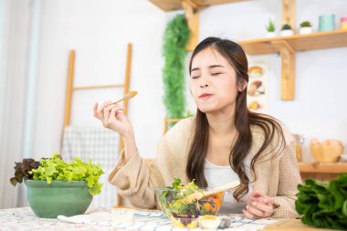 Gülümseyen kadın taze sağlıklı salata sebzeleri yiyor. Güzel bir iç mutfakta kilerde oturan bir kadın. Yerel ürünlerden ve malzemelerden alınan temiz diyet gıdaları taze pazardır..
