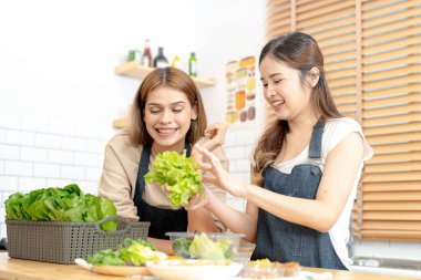 Gülümseyen kadınlar taze sağlıklı salata sebzeleri hazırlıyorlar. Güzel bir iç mutfakta kilerde oturan bir kadın. Yerel ürünlerden ve malzemelerden alınan temiz diyet gıdaları taze pazardır..