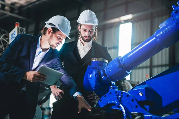 Business engineers meet and check control heavy machine robot arm. Diverse Team of Industrial Robotics Engineers Gathered Around machine. Professional Machinery Operator Use Industrial Digital Tablet.