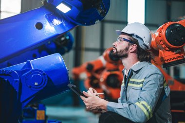 Fabrika mühendisi akıllı tabletle makineyi inceliyor. İşçi Heavy Machine Robot Kol 'da çalışıyor. Endüstriyel bir fabrikada uzaktan kumandalı kaynak makinesi. Yapay zeka kavramı.