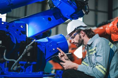 Fabrika mühendisi akıllı tabletle makineyi inceliyor. İşçi Heavy Machine Robot Kol 'da çalışıyor. Endüstriyel bir fabrikada uzaktan kumandalı kaynak makinesi. Yapay zeka kavramı.