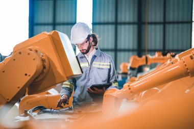 Fabrika mühendisi akıllı tabletle makineyi inceliyor. İşçi Heavy Machine Robot Kol 'da çalışıyor. Endüstriyel bir fabrikada uzaktan kumandalı kaynak makinesi. Yapay zeka kavramı.