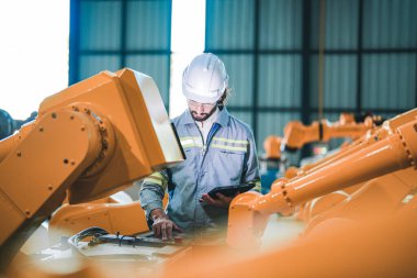 Fabrika mühendisi akıllı tabletle makineyi inceliyor. İşçi Heavy Machine Robot Kol 'da çalışıyor. Endüstriyel bir fabrikada uzaktan kumandalı kaynak makinesi. Yapay zeka kavramı.