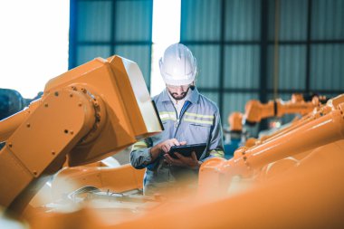 Fabrika mühendisi akıllı tabletle makineyi inceliyor. İşçi Heavy Machine Robot Kol 'da çalışıyor. Endüstriyel bir fabrikada uzaktan kumandalı kaynak makinesi. Yapay zeka kavramı.