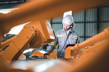 Fabrika mühendisi akıllı tabletle makineyi inceliyor. İşçi Heavy Machine Robot Kol 'da çalışıyor. Endüstriyel bir fabrikada uzaktan kumandalı kaynak makinesi. Yapay zeka kavramı.