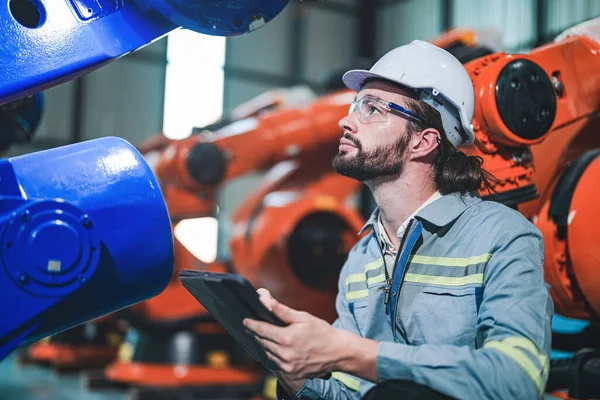 Factory engineer inspecting on machine with smart tablet. Worker works at heavy machine robot arm. The welding machine with a remote system in an industrial factory. Artificial intelligence concept.