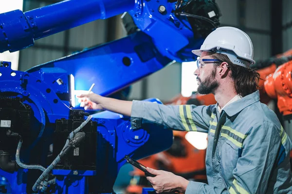 Factory engineer inspecting on machine with smart tablet. Worker works at heavy machine robot arm. The welding machine with a remote system in an industrial factory. Artificial intelligence concept.