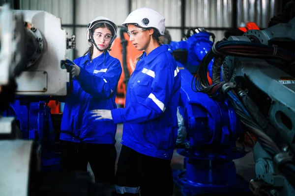 Factory engineer women inspecting on machine with smart tablet. Worker works at machine robot arm. The welding machine with a remote system in an industrial factory. Artificial intelligence concept.