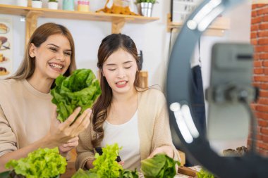 Genç kadın blogcular sağlık hizmetleri için sağlıklı gıda salatası gösteriyor. Akıllı cep telefonu kullanan ekip online olarak kilo vermek için sağlıklı gıda satıyor..