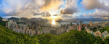 Hong Kong 'un gökyüzü ve günbatımlı şehir manzarası. Yüksek binaların, modern kulelerin ve gökyüzünün limana yansıyan muhteşem manzarası. Hong Kong adası ve Kowloon kıyısı..
