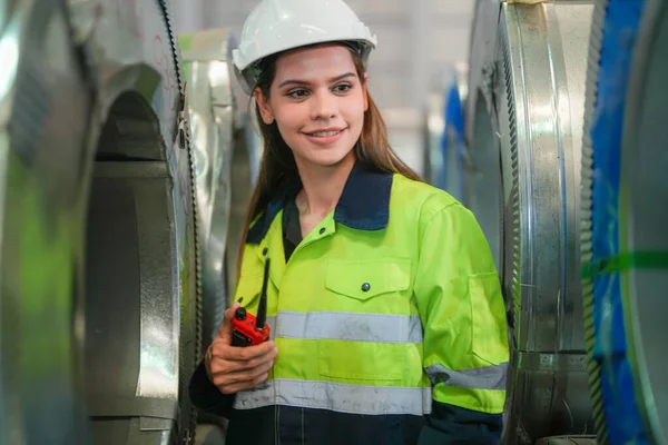 女工程师自信地站在钢制角色扮演材料仓库前 身穿绿色工作服 头戴安全帽 精明的工业工人 — 图库照片