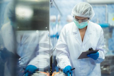 Kadın fabrika işçileri endüstriyel fabrikadaki makine sistemlerini kontrol ediyorlar. Kadınlar içecek ve gıda üretimi için temiz odalarda çalışıyorlar