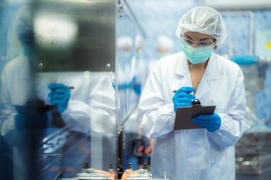 Kadın fabrika işçileri endüstriyel fabrikadaki makine sistemlerini kontrol ediyorlar. Kadınlar içecek ve gıda üretimi için temiz odalarda çalışıyorlar