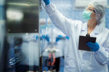 Kadın fabrika işçileri endüstriyel fabrikadaki makine sistemlerini kontrol ediyorlar. Kadınlar içecek ve gıda üretimi için temiz odalarda çalışıyorlar