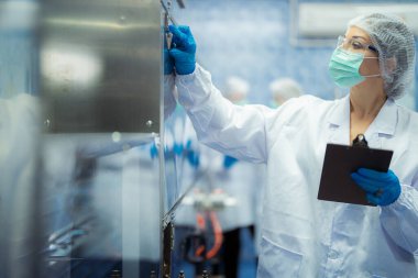 Kadın fabrika işçileri endüstriyel fabrikadaki makine sistemlerini kontrol ediyorlar. Kadınlar içecek ve gıda üretimi için temiz odalarda çalışıyorlar