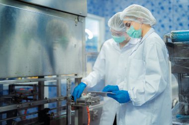 Kadın fabrika işçileri endüstriyel fabrikadaki makine sistemlerini kontrol ediyorlar. Kadınlar içecek ve gıda üretimi için temiz odalarda çalışıyorlar