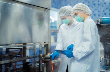 Kadın fabrika işçileri endüstriyel fabrikadaki makine sistemlerini kontrol ediyorlar. Kadınlar içecek ve gıda üretimi için temiz odalarda çalışıyorlar