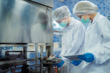 Kadın fabrika işçileri endüstriyel fabrikadaki makine sistemlerini kontrol ediyorlar. Kadınlar içecek ve gıda üretimi için temiz odalarda çalışıyorlar