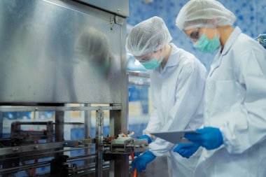 Kadın fabrika işçileri endüstriyel fabrikadaki makine sistemlerini kontrol ediyorlar. Kadınlar içecek ve gıda üretimi için temiz odalarda çalışıyorlar