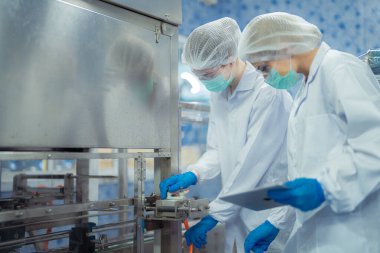 Kadın fabrika işçileri endüstriyel fabrikadaki makine sistemlerini kontrol ediyorlar. Kadınlar içecek ve gıda üretimi için temiz odalarda çalışıyorlar