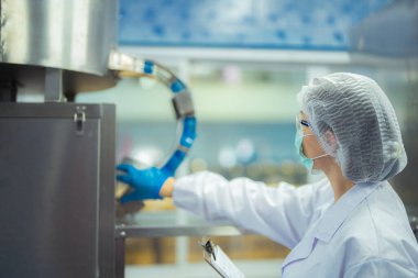 Kadın fabrika işçisi endüstriyel fabrikadaki makine sistemlerini kontrol ediyor. Kadın içecek ve gıda üretimi için temiz odalarda çalışıyor.