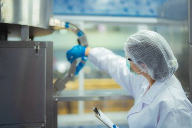 Kadın fabrika işçisi endüstriyel fabrikadaki makine sistemlerini kontrol ediyor. Kadın içecek ve gıda üretimi için temiz odalarda çalışıyor.