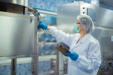 Kadın fabrika işçisi endüstriyel fabrikadaki makine sistemlerini kontrol ediyor. Kadın içecek ve gıda üretimi için temiz odalarda çalışıyor.