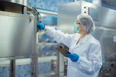 Kadın fabrika işçisi endüstriyel fabrikadaki makine sistemlerini kontrol ediyor. Kadın içecek ve gıda üretimi için temiz odalarda çalışıyor.