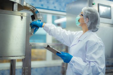 Kadın fabrika işçisi endüstriyel fabrikadaki makine sistemlerini kontrol ediyor. Kadın içecek ve gıda üretimi için temiz odalarda çalışıyor.