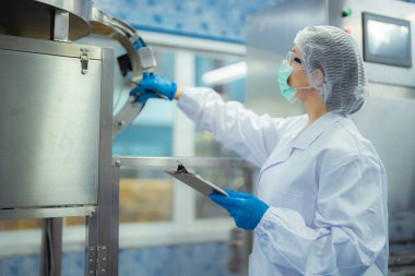 Kadın fabrika işçisi endüstriyel fabrikadaki makine sistemlerini kontrol ediyor. Kadın içecek ve gıda üretimi için temiz odalarda çalışıyor.