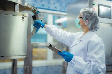 Kadın fabrika işçisi endüstriyel fabrikadaki makine sistemlerini kontrol ediyor. Kadın içecek ve gıda üretimi için temiz odalarda çalışıyor.