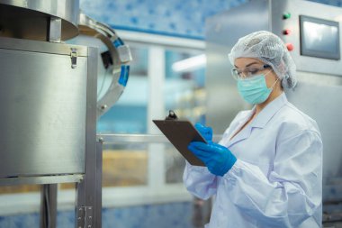 Kadın fabrika işçisi endüstriyel fabrikadaki makine sistemlerini kontrol ediyor. Kadın içecek ve gıda üretimi için temiz odalarda çalışıyor.