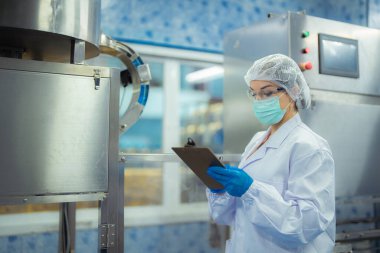 Kadın fabrika işçisi endüstriyel fabrikadaki makine sistemlerini kontrol ediyor. Kadın içecek ve gıda üretimi için temiz odalarda çalışıyor.