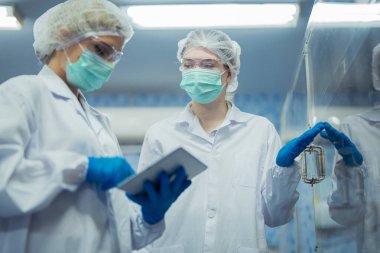 Kadın fabrika işçileri endüstriyel fabrikadaki makine sistemlerini kontrol ediyorlar. Kadınlar içecek ve gıda üretimi için temiz odalarda çalışıyorlar