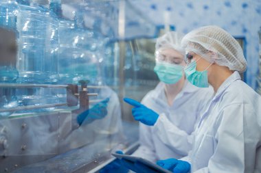 Bilim adamı, endüstriyel fabrikanın makine taşıma hattındaki su şişelerinin kalitesini kontrol ediyor. İçki üretim hattında veri kaydeden kadın işçi..