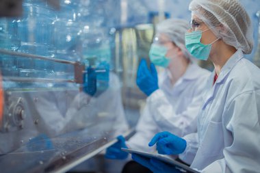 Bilim adamı, endüstriyel fabrikanın makine taşıma hattındaki su şişelerinin kalitesini kontrol ediyor. İçki üretim hattında veri kaydeden kadın işçi..