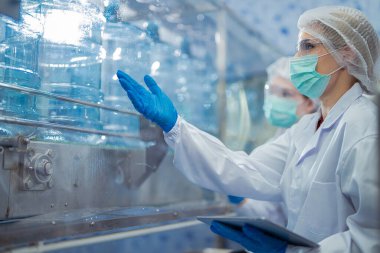 Bilim adamı, endüstriyel fabrikanın makine taşıma hattındaki su şişelerinin kalitesini kontrol ediyor. İçki üretim hattında veri kaydeden kadın işçi..